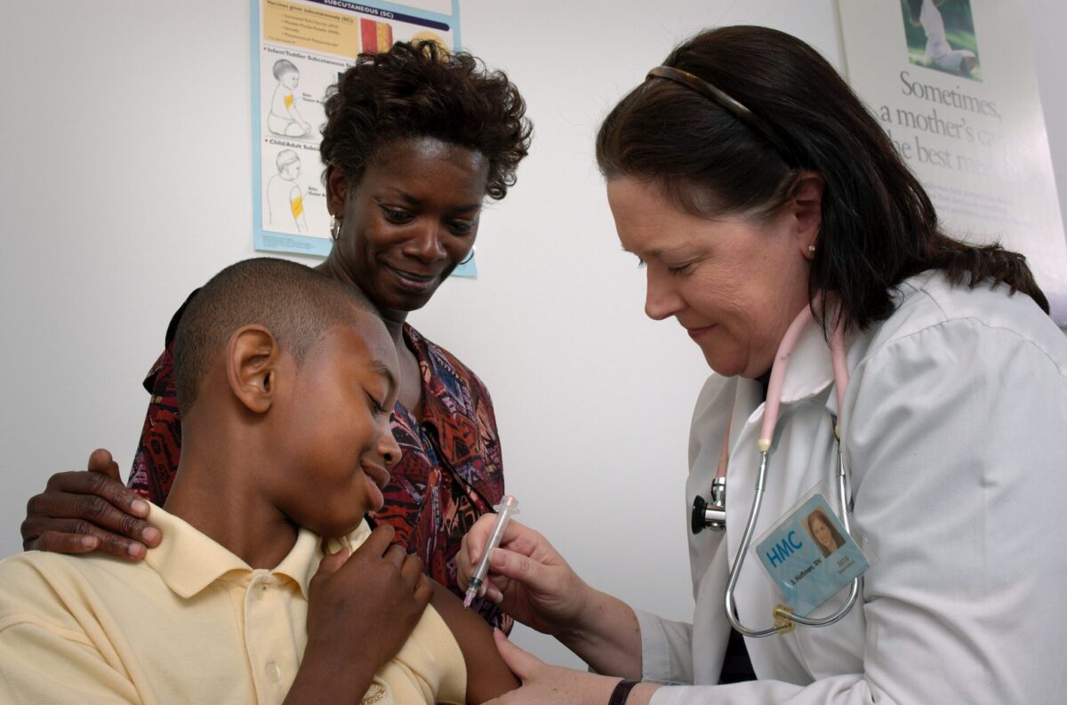 Teenage boy and mother smile as a nurse vaccinates him